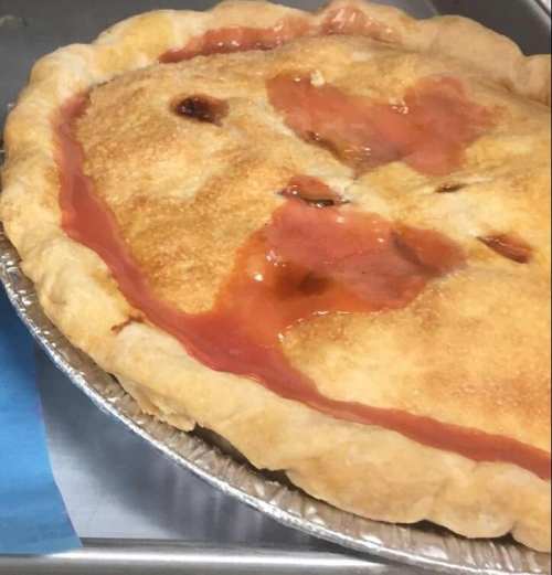 A freshly baked pie with a golden crust and a glossy, fruit-filled interior, resting in a silver pie dish.