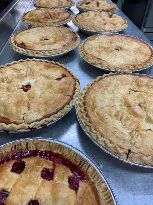 Freshly baked pies cooling on a metal surface, featuring golden crusts and visible fruit filling.