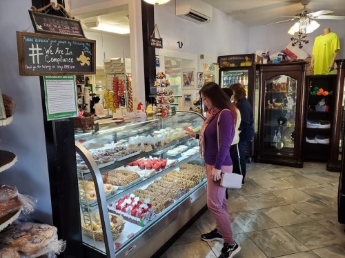 A woman examines a display case filled with various pastries and desserts in a cozy shop.
