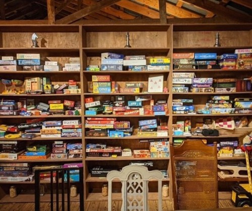 A wooden shelf filled with various board games, neatly organized in rows, with a cozy, rustic setting.