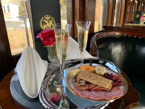 A silver tray holds a charcuterie platter with meats, cheeses, and crackers, alongside two flutes of champagne and a rose.