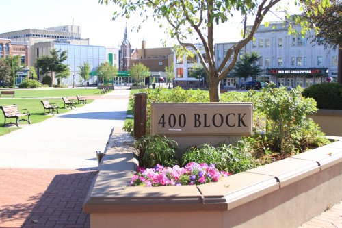 Sign for "400 Block" in a park setting with benches, flowers, and buildings in the background on a sunny day.