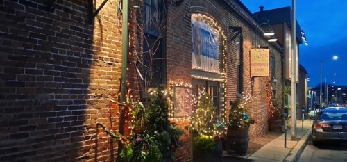 A cozy brick building adorned with string lights and greenery, illuminated at dusk.