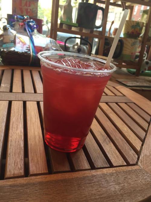 A clear cup filled with a red beverage and ice, sitting on a wooden table.