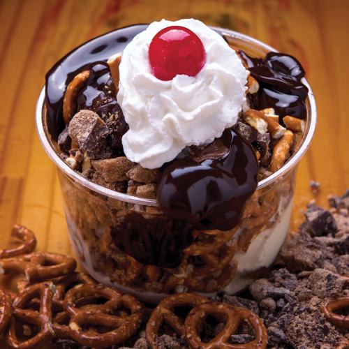 A dessert cup filled with ice cream, crushed pretzels, chocolate sauce, whipped cream, and a cherry on top.