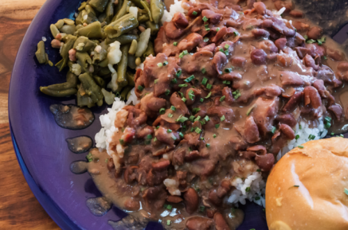 A plate of rice topped with red beans and gravy, served with green beans and a bread roll on the side.