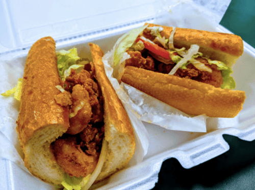 Two sandwiches filled with fried chicken, lettuce, and tomato, served in a takeout container.