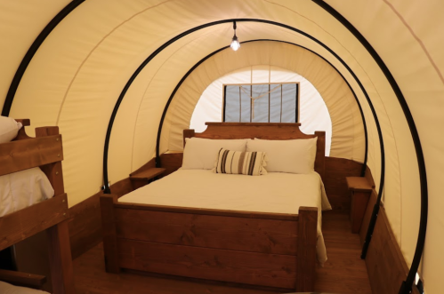 Cozy interior of a glamping tent featuring a wooden bed, bedside tables, and warm lighting.