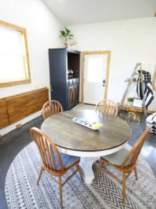 A cozy dining area featuring a round wooden table, four chairs, and a door leading outside, with decorative elements.