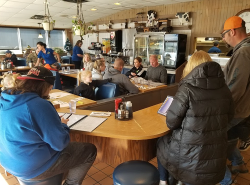 A busy diner scene with people seated at a counter and tables, enjoying meals and chatting in a cozy atmosphere.