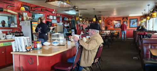 A cozy diner with red walls, a man in a hat reading a menu, and staff serving customers in a warm atmosphere.