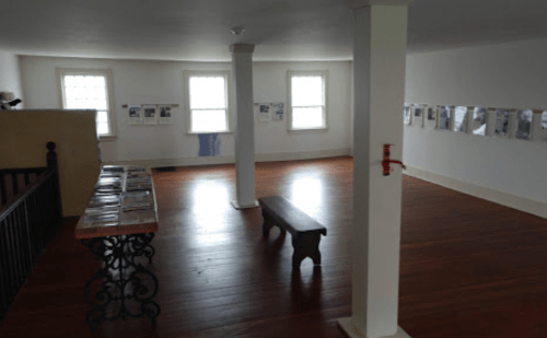 Interior of a gallery with wooden floors, a bench, and walls displaying framed photographs and information.