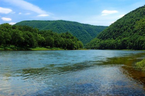 A serene river flows between lush green mountains under a clear blue sky.