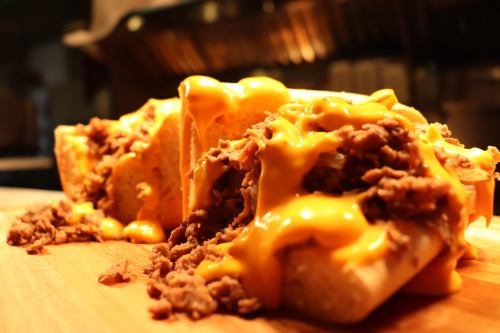 A close-up of a cheesy sandwich filled with shredded meat, resting on a wooden cutting board.