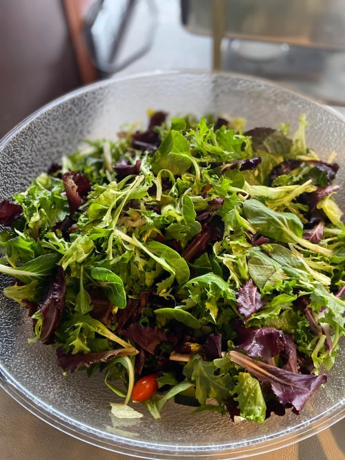 A clear bowl filled with a fresh green salad, featuring various leafy greens and a hint of red cherry tomatoes.