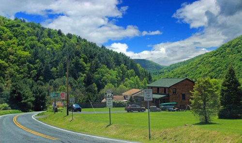 A scenic view of a winding road with green hills, a wooden building, and blue skies with fluffy clouds.