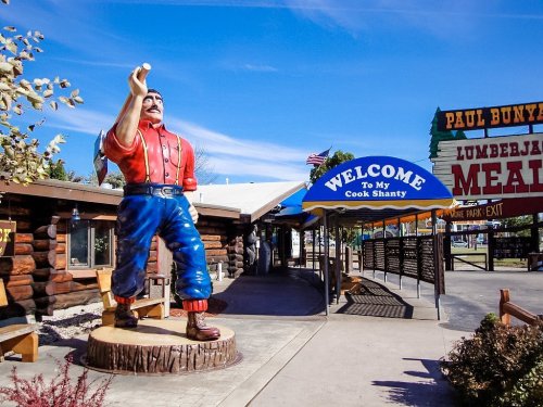 A large statue of Paul Bunyan stands outside a log cabin entrance with a sign that reads "Welcome To My Cook Shanty."