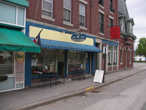 A quaint street scene featuring a blue and yellow café with outdoor seating and nearby brick buildings.