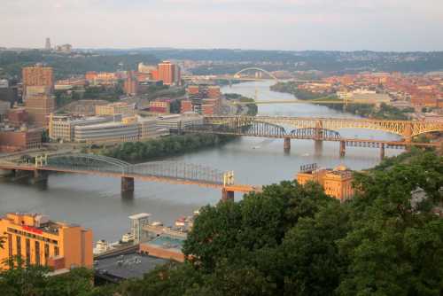 A panoramic view of Pittsburgh, featuring rivers, bridges, and city buildings under a clear sky.