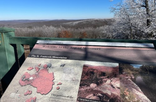 A scenic view from a lookout point with a sign about the St. Francois Mountains in Missouri, surrounded by frosty trees.
