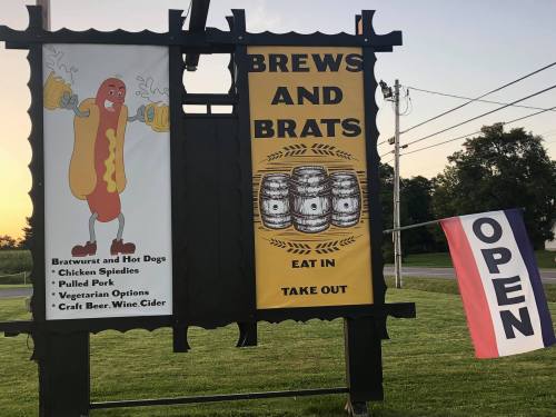 Sign advertising "Brews and Brats" with images of hot dogs and barrels, featuring options for takeout and dining.