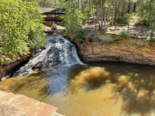 A serene waterfall cascades into a calm pool, surrounded by lush greenery and rocky cliffs.