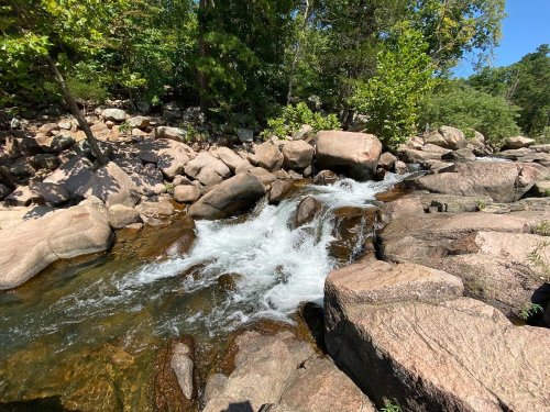 A rocky stream flows through a lush green landscape under a clear blue sky.