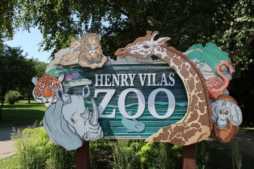 Colorful sign for Henry Vilas Zoo featuring illustrations of a lion, tiger, giraffe, rhino, flamingo, and other animals.