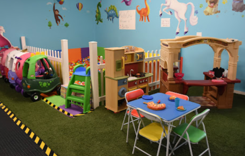 Colorful play area with a toy kitchen, table, and a train-shaped play structure against a vibrant wall.