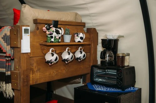Cozy interior with a wooden bed, cow-themed mugs, a coffee maker, and a toaster oven in a tent-like setting.