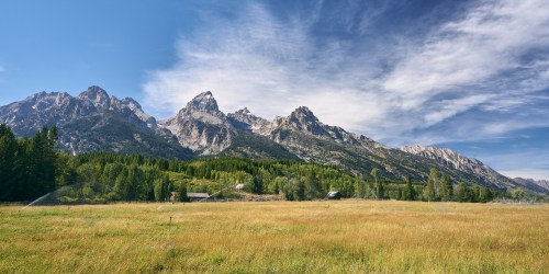 A scenic view of mountains under a blue sky, with a grassy field and trees in the foreground.
