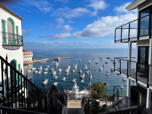 A scenic view of a harbor filled with boats, framed by buildings and a blue sky with scattered clouds.