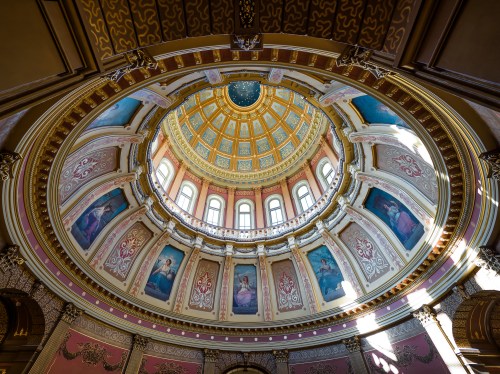 A view of a beautifully decorated dome with intricate designs and paintings, illuminated by natural light.