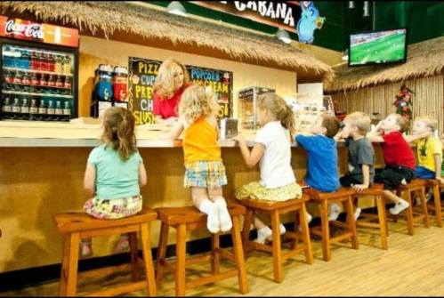 A group of children sitting at a counter in a colorful snack bar, with a staff member serving them.