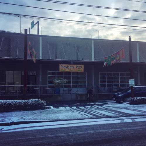 Exterior of PlayDate PDX building with snow on the ground and colorful flags hanging outside.