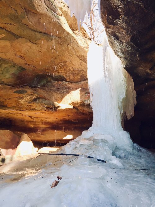 A frozen waterfall inside a cave, with icicles hanging from the rocky ceiling and water dripping down.