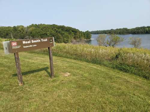 Sign for Neal Smith Trail near Saydel Lake, with grassy area and trees in the background. Calm water visible.