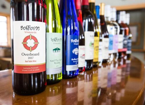 A row of wine bottles on a wooden table, featuring various labels and colors, including red, white, and rosé wines.