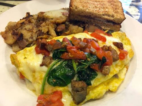 A plate of a cheesy omelette topped with spinach and tomatoes, served with hash browns and toasted bread.