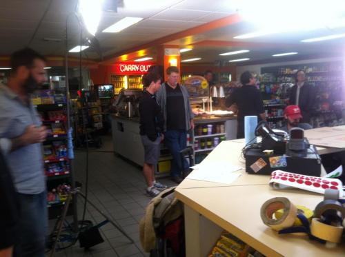 A busy convenience store with people interacting, shelves stocked with snacks, and a counter with various items.