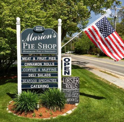 Sign for Marion's Pie Shop featuring menu items, an "Open" notice, and an American flag in the background.