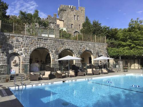 A serene pool area with lounge chairs, umbrellas, and a stone castle in the background under a clear blue sky.