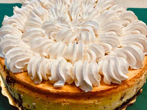 A creamy cheesecake topped with swirls of whipped cream, displayed on a golden cake board.