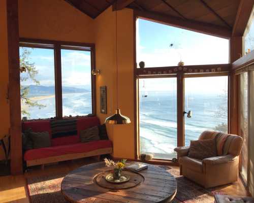 Cozy living room with a red sofa and armchair, large windows showcasing a scenic ocean view and blue sky.