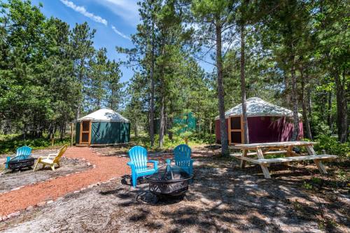 Two colorful yurts surrounded by trees, with a fire pit and picnic table in a natural setting.
