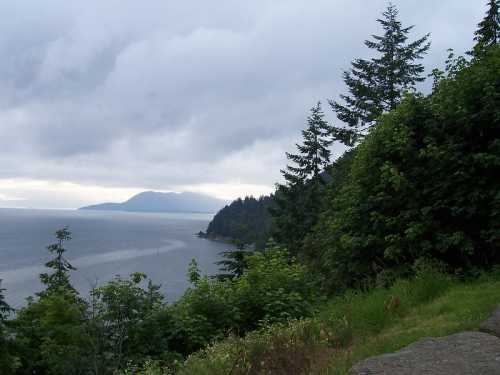 A scenic view of a cloudy coastline with lush greenery and distant mountains across the water.