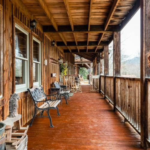 A wooden porch with rocking chairs and potted plants, surrounded by rustic wooden walls and a scenic view.