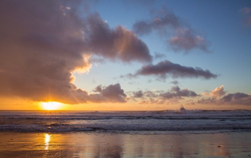 A serene beach at sunset, with vibrant colors in the sky and gentle waves lapping at the shore.