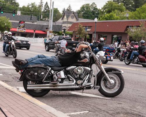 A motorcyclist reclines on their bike at an intersection, surrounded by other motorcycles and shops in the background.
