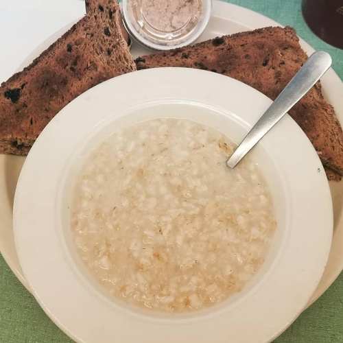 A bowl of oatmeal with a spoon, accompanied by two slices of dark bread on a plate.